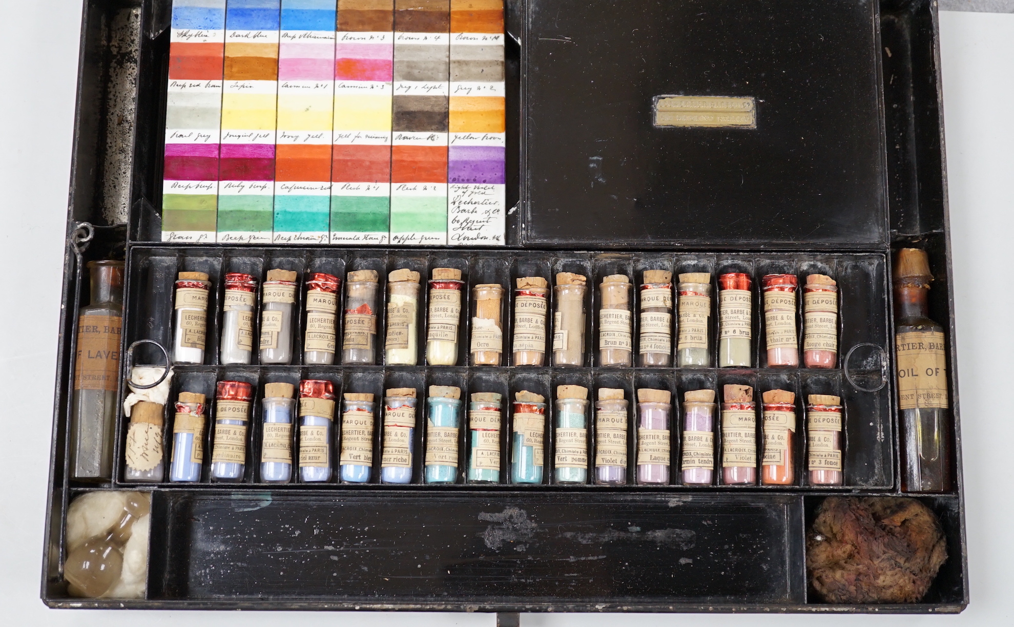 A black artist's tin box, with fitted interior, containing glass phialls of coloured shades of powdered paint and a white glass samples panel etc, box 37.5cm wide, 27cm deep